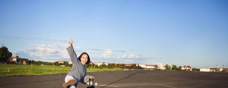 無料Photo 幸せなアジアのスケート選手の女の子がスケートボードと笑顔の女性のスケートで立ってジャンプする垂直ショット
