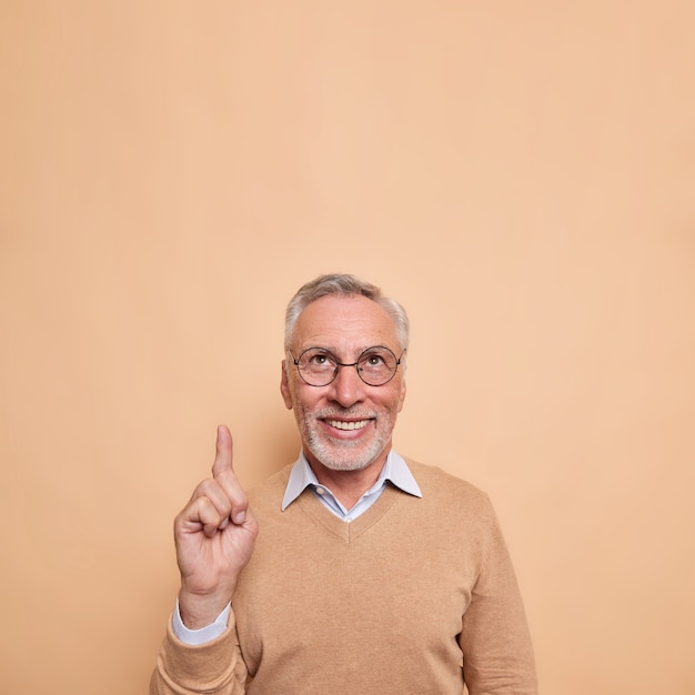 Вертикальный снимок счастливого бородатого зрелого мужчины с указательным пальцем выше показывает пустое пространство