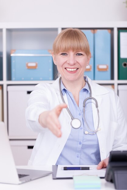 Vertical shot of a happy Caucasian doctor offering cooperation with a handshake