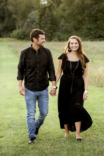 Vertical shot of happy couple holding hands while walking on grassy field