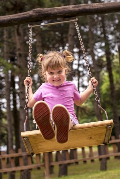 Vertical shot of a happy female child swinging behind the trees