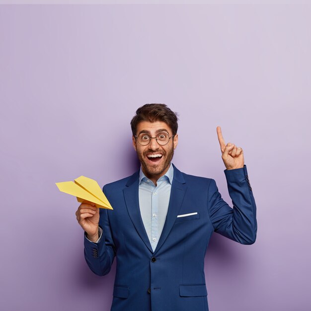 Vertical shot of happy male director in elegant formal wear, points index finger above