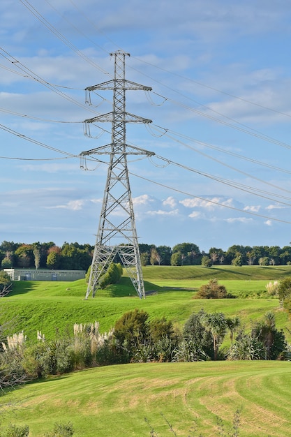 Вертикальный снимок высоковольтной электрической башни с зеленым лугом на переднем плане