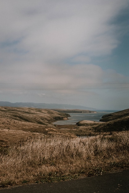 Free photo vertical shot of hills and grass by the body of water under a cloudy sky