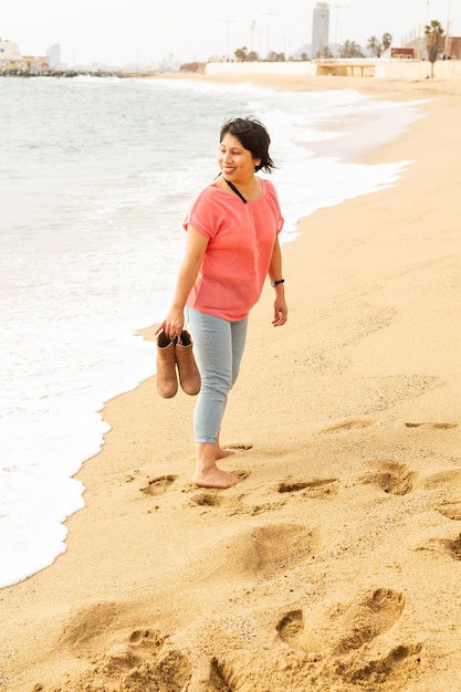 스페인 바르셀로나 바르셀로네타 해변에서 모래 위를 걷고 있는 히스패닉계 여성의 세로 샷