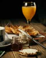 Free photo vertical shot of honey and orange juice and a knife spreading cream on a slice of bread on a table