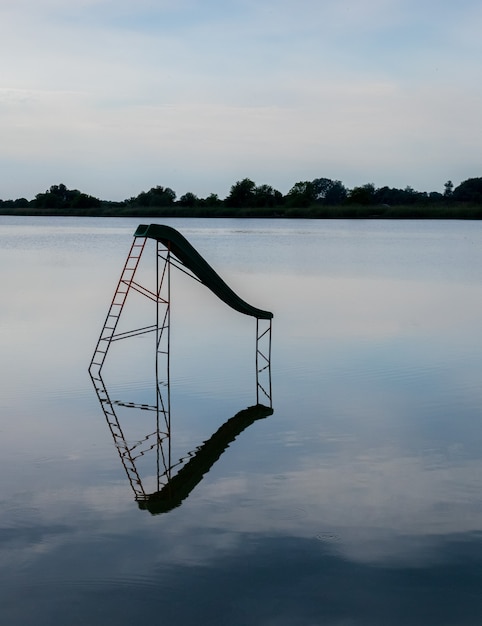 Vertical shot of a lake with a water swing reflected in the water and trees on the background