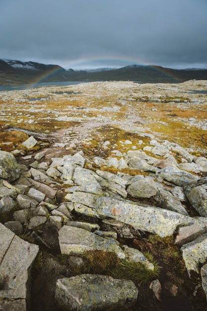 Vertical shot of land with a lot of rock formations and the rainbow in background in Finse, Norway