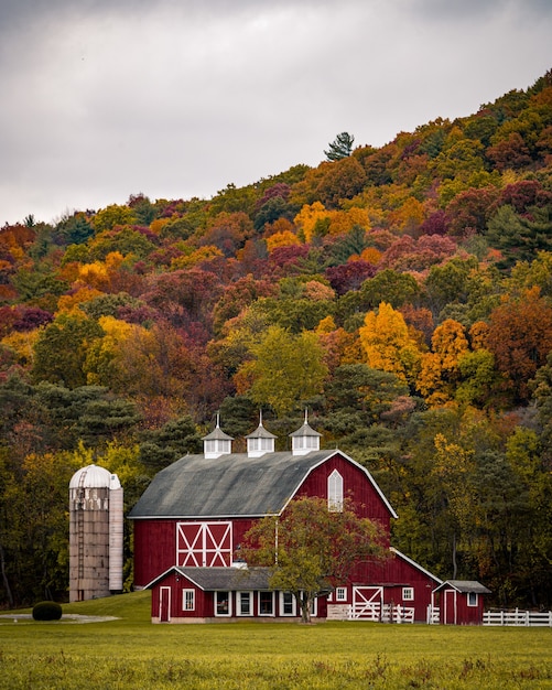 Vertical shot of a large barn near a hill with colorful autumn trees