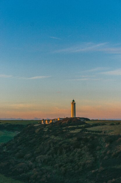 Vertical shot of a lighthouse on top of a hill under a sunset sky