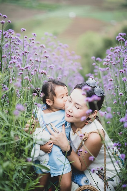 美しい紫色の花でフィールドで彼女の母親にキスする小さなアジアの女の子の垂直ショット