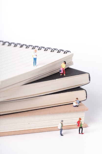 Free photo vertical shot of little figurines of students standing on and around textbooks