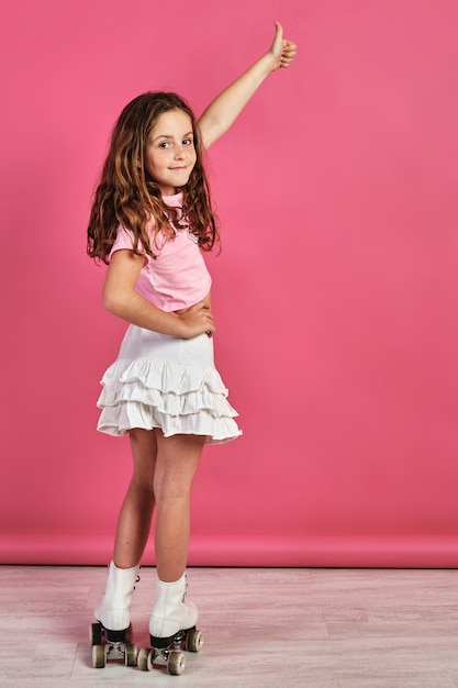 Foto gratuita colpo verticale di una bambina in pattini a rotelle in posa e gesticolando il segno simile