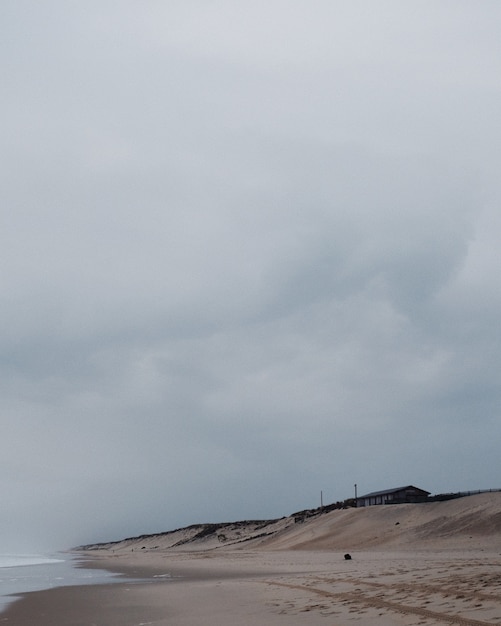 Foto gratuita colpo verticale di una casa solitaria sulla spiaggia sotto il cielo nuvoloso