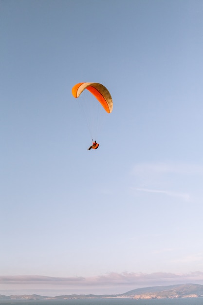 美しい青い空の下をパラシュートで下る孤独な人の垂直方向のショット