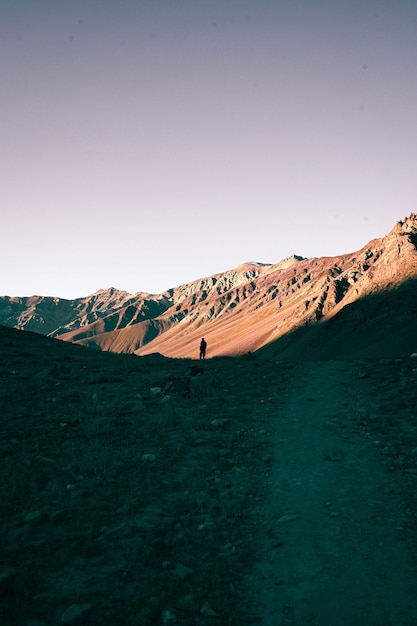 Foto gratuita colpo verticale di una persona sola che cammina in montagna durante il tramonto