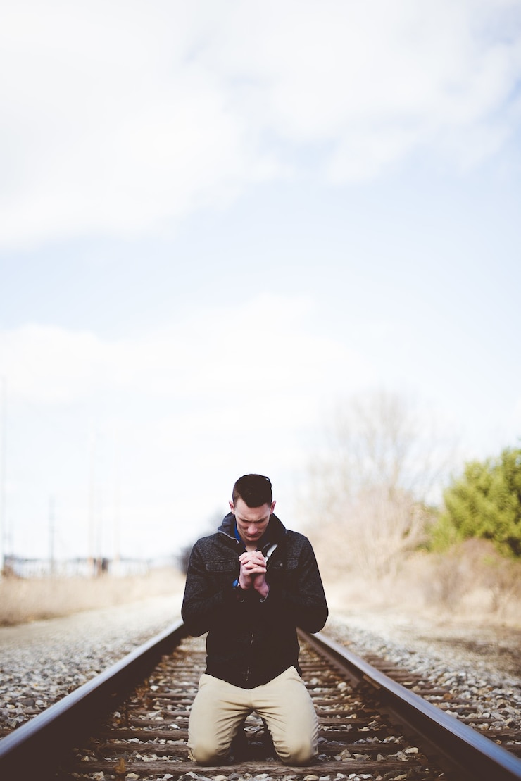 Free Photo vertical shot of a male on his knees on train tracks and praying while his eyes are closed