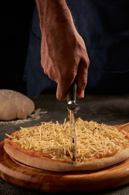 チーズとトウモロコシでおいしいピザをピザナイフで切る男性の手の垂直ショット