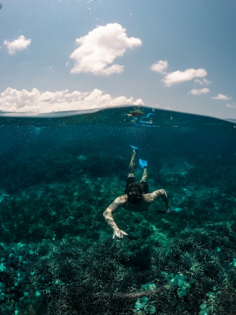 Vertical shot of male swimming underwater with the sky in the background