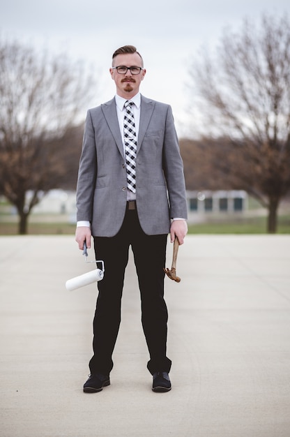 Vertical shot of a male wearing a suit while holding a hammer and a paintbrush on the street