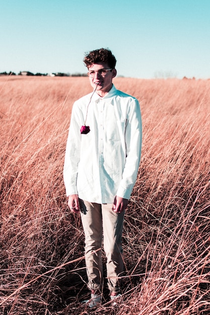 Vertical shot of a male wearing a white shirt with a rose in his mouth