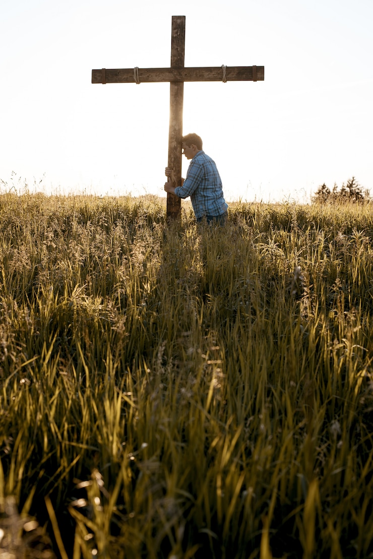 Free Photo vertical shot of a male with his head against a wooden cross in a grassy field