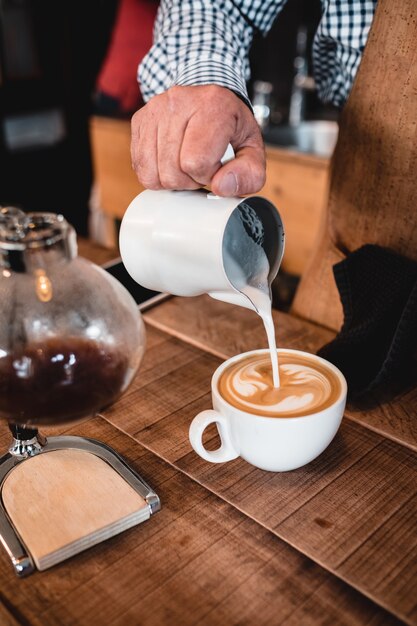 Vertical shot man pouring milk into cappuccino