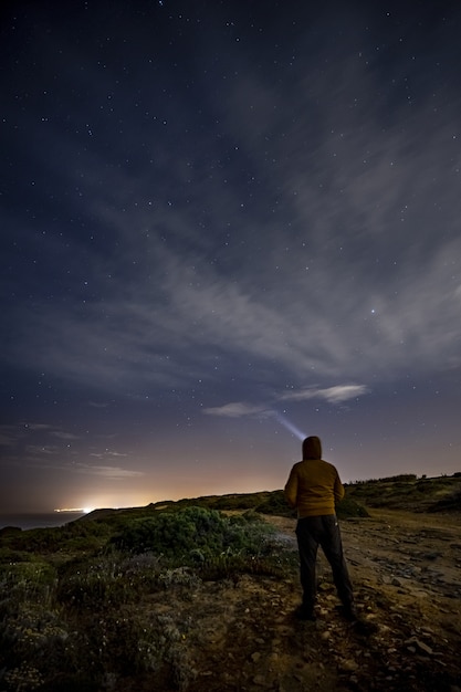 岩の上に立って、夜に輝く星を見ている男の垂直ショット
