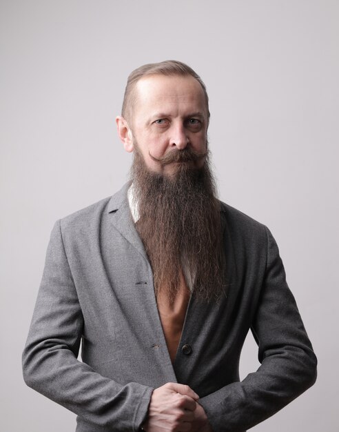 Vertical shot of a man with a long beard and a mustache standing in front of a grey wall