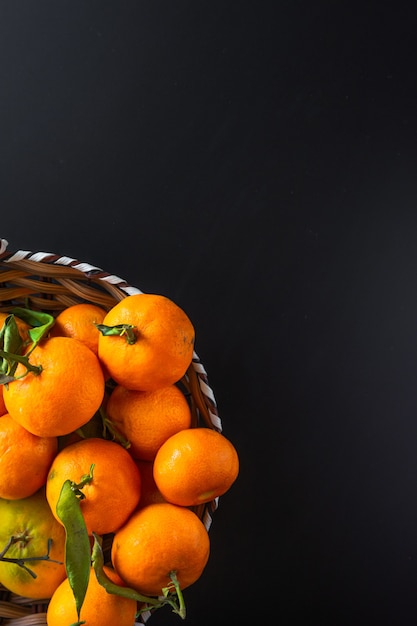 Vertical shot of mandarins with green leaves on black