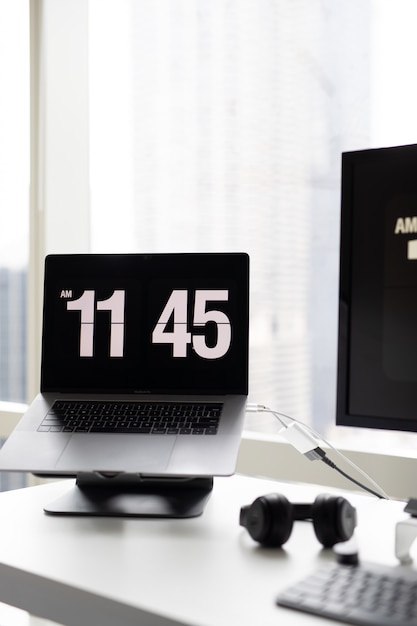 Vertical shot of a modern laptop showing the time with headphones on the side on the desk