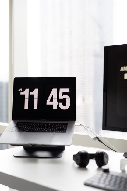 Вертикальный снимок современного ноутбука, показывая время с наушниками на стороне на столе