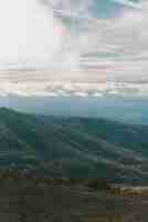 Foto gratuita colpo verticale delle montagne sotto un cielo nuvoloso blu