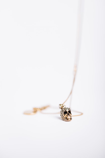 Vertical shot of a necklace with a skull-like charm on white background
