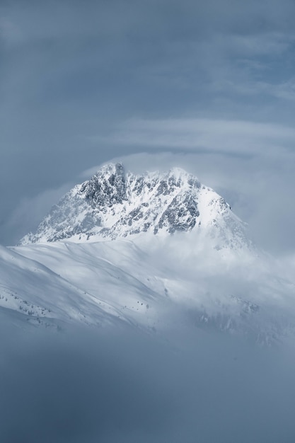 Бесплатное фото Вертикальный выстрел красивый скалистый холм, покрытый снегом, окутанный туманом