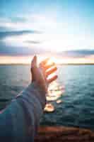 無料写真 太陽の下で美しい海を背景にした手の垂直ショット
