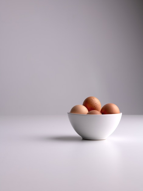 無料写真 白い表面と灰色のきれいな背景に茶色の卵が入った白いボウルの垂直ショット