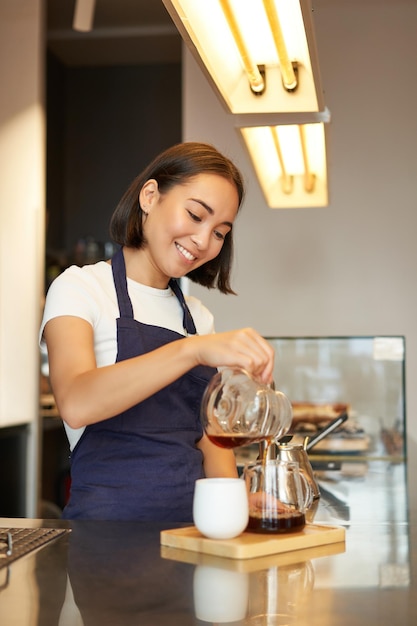 無料写真 バリスタとして働いている笑顔の女の子の垂直ショットは、フィルター コーヒー バッチ醸造 s を作る上に注ぐ準備します。