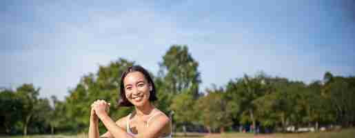 無料写真 満足して微笑む脚にストレッチバンドを使用して公園でスクワットをする若い健康な女性の垂直ショット