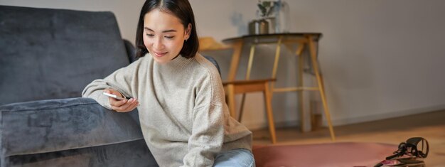 무료 사진 스마트폰을 사용하고 커피를 마시는 아늑한 집에서 노트북 작업을 하는 젊은 여성의 세로 샷