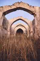 Free photo vertical shot of an old ancient ruin with an arched ceiling in a dry grassy field under a blue sky