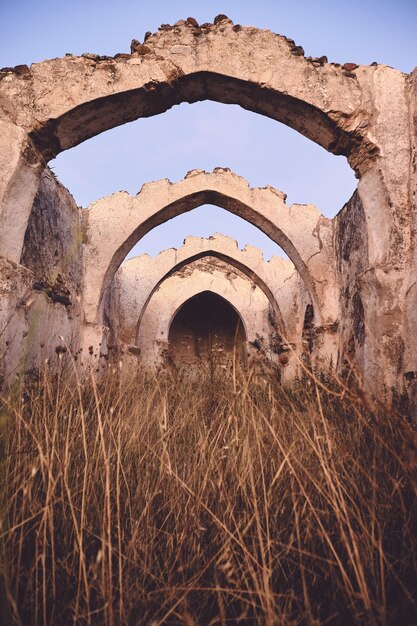 Vertical shot of an old ancient ruin with an arched ceiling in a dry grassy field under a blue sky