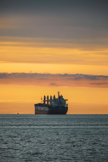 Vertical shot of the old ship in a lake under the colorful sky during sunset