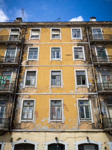 Vertical shot of an old yellow-painted apartment building with some broken windows