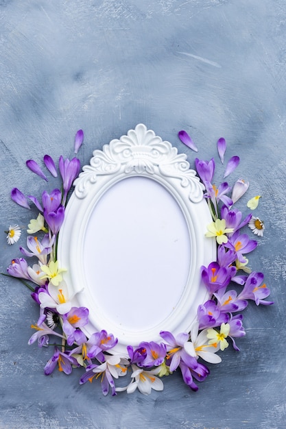 Foto gratuita colpo verticale di una cornice bianca decorata con fiori primaverili viola e bianchi