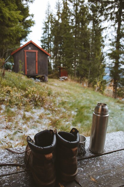 Vertical shot of a pair of boots and a flask near a wooden cottage in the forest in Norway