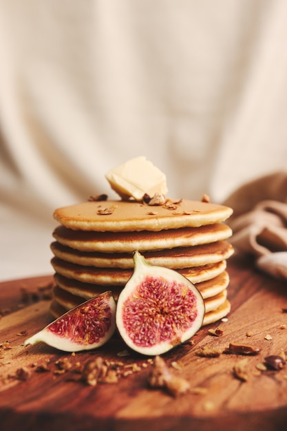 Vertical shot of pancakes with syrup, butter, figs and roasted nuts on a wooden plate