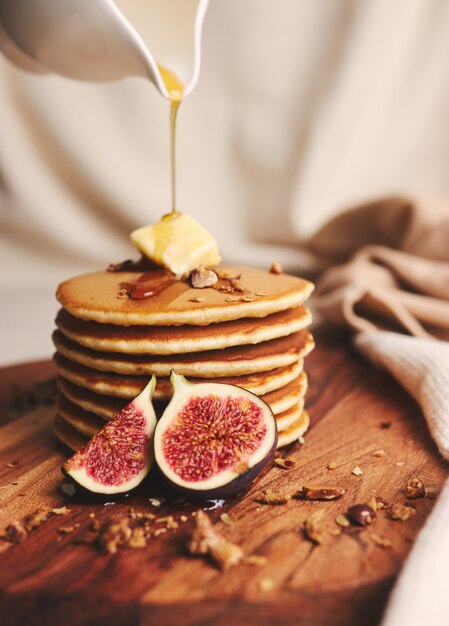 Vertical shot of pancakes with syrup, butter and roasted nuts on a wooden plate