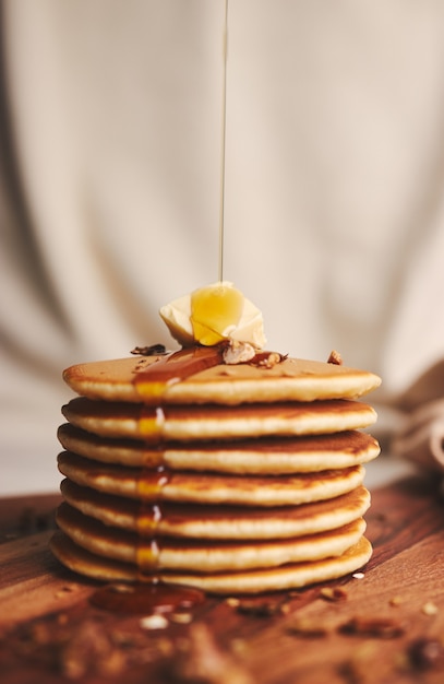 Вертикальный снимок блинов с сиропом, маслом и жареными орехами на деревянной тарелке