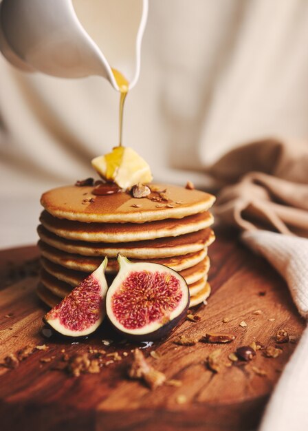 Вертикальный снимок блинов с сиропом, маслом и жареными орехами на деревянной тарелке